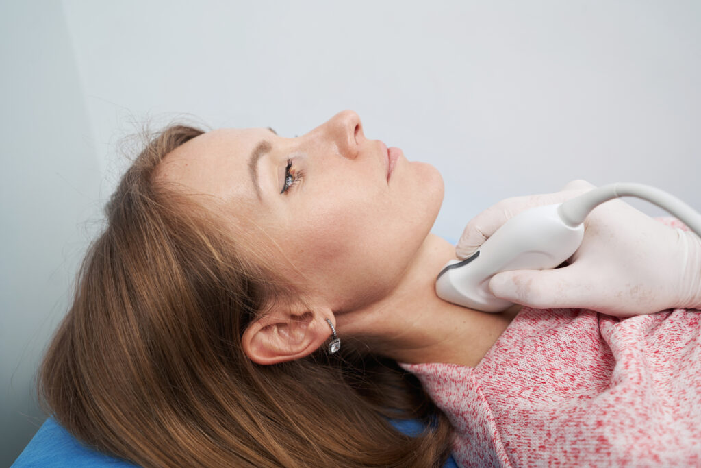 Endocrinologist wearing white gloves scanning the thyroid gland of Caucasian woman lying on couch in office